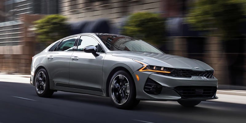 Silver Kia sedan driving on a city street with blurred background