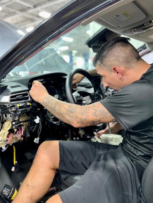 Technician working inside a vehicle cabin, handling dashboard wiring and interior electronics