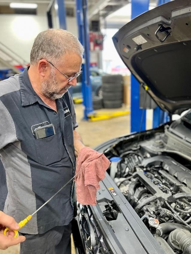 Technician checking the oil level of a vehicle using a dipstick and a cloth in an auto repair garage