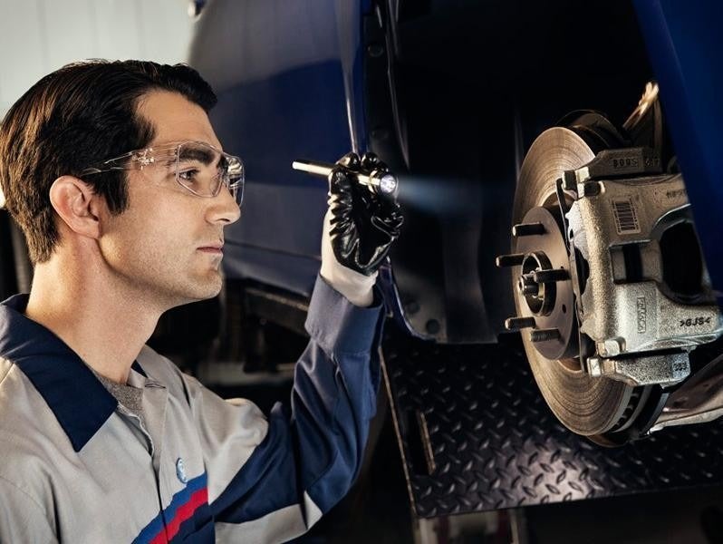 Technician inspecting a car brake system using a flashlight while wearing safety glasses and gloves