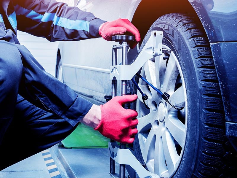 Mechanic performing a wheel alignment on a car using specialized equipment while wearing red gloves